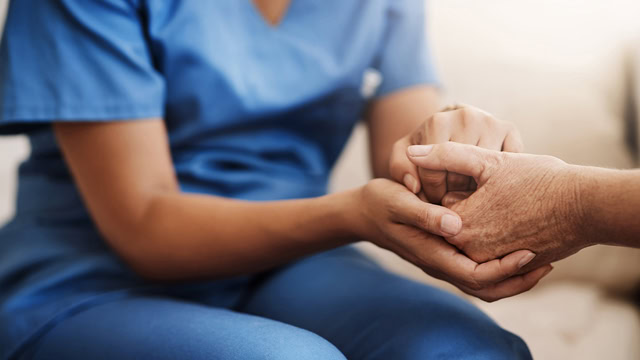 African American caregiver and senior woman holding hands for support.