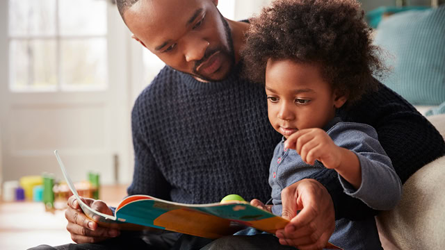 African American father and son reading a book together at home.