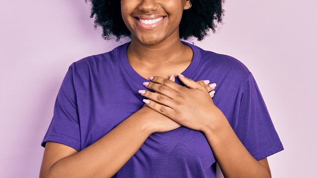 African American female smiling with her hands on her heart.