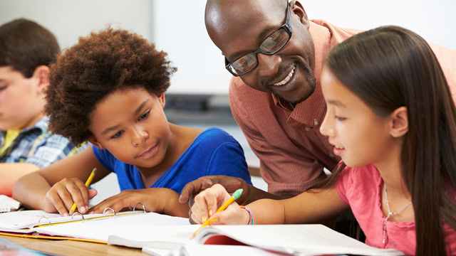 African American teacher helping diverse students studying in a classroom.