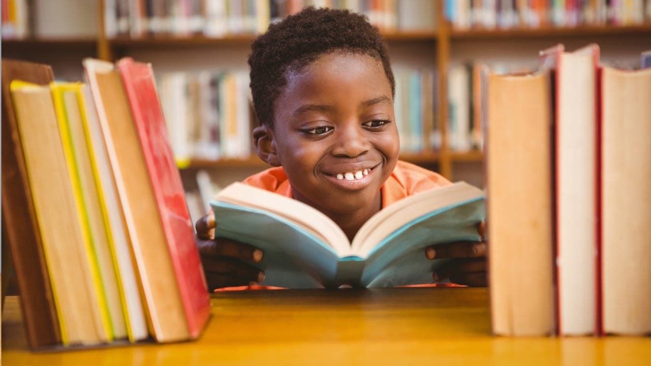 African-American youth reading a book in front of a bookshelf at New Jersey library.