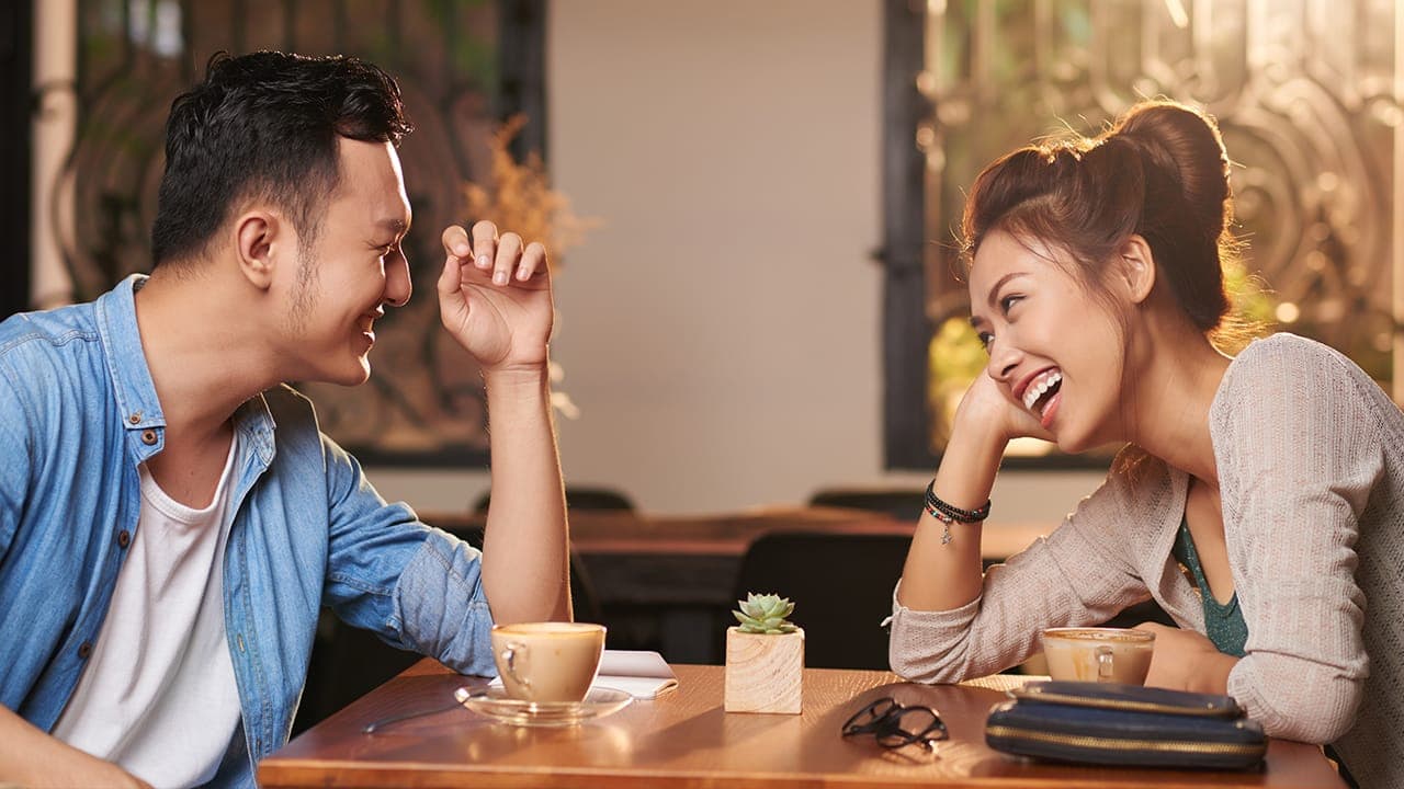 Asian couple laughing while on a date at New Jersey bar restaurant.