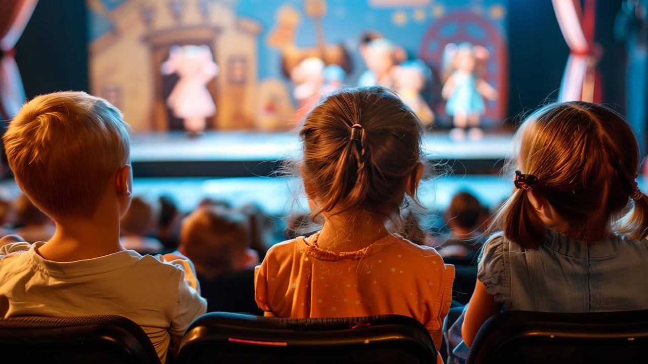 Audience of children sitting in theater watching live stage performance. Image produced by More Jersey.