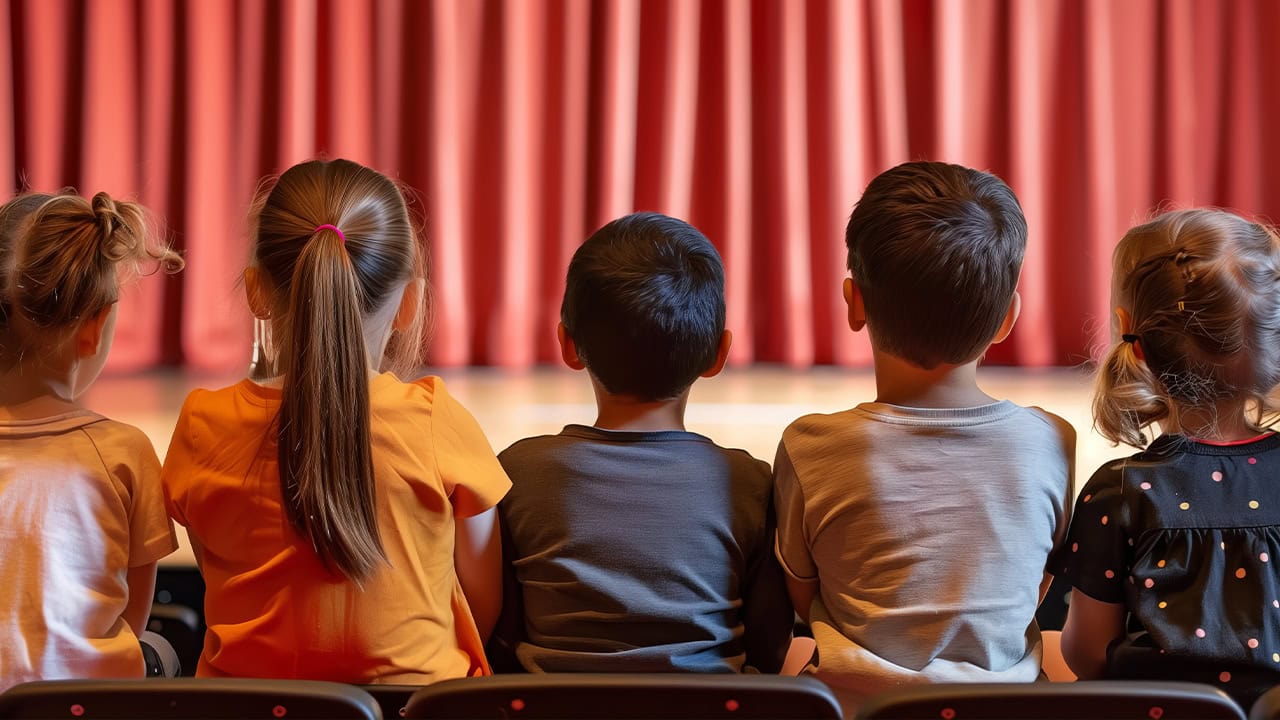 Audience of children sitting in theater watching live stage performance. Image produced by More Jersey.