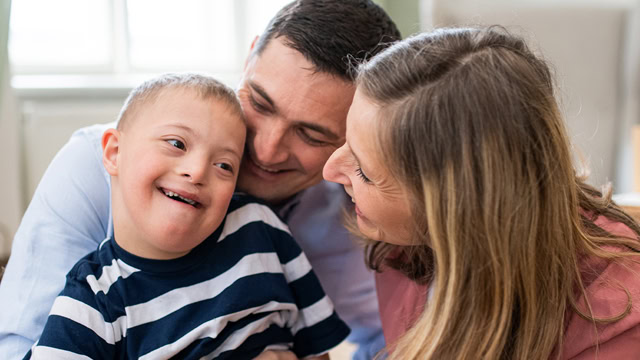 Cheerful down syndrome boy with parents hugging at home.