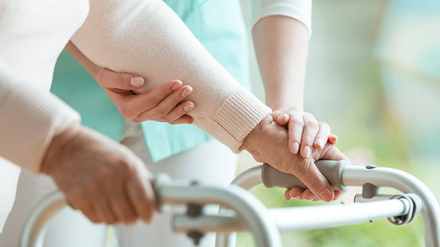 Close-up of a caregiver helping a senior woman walk with her walker.