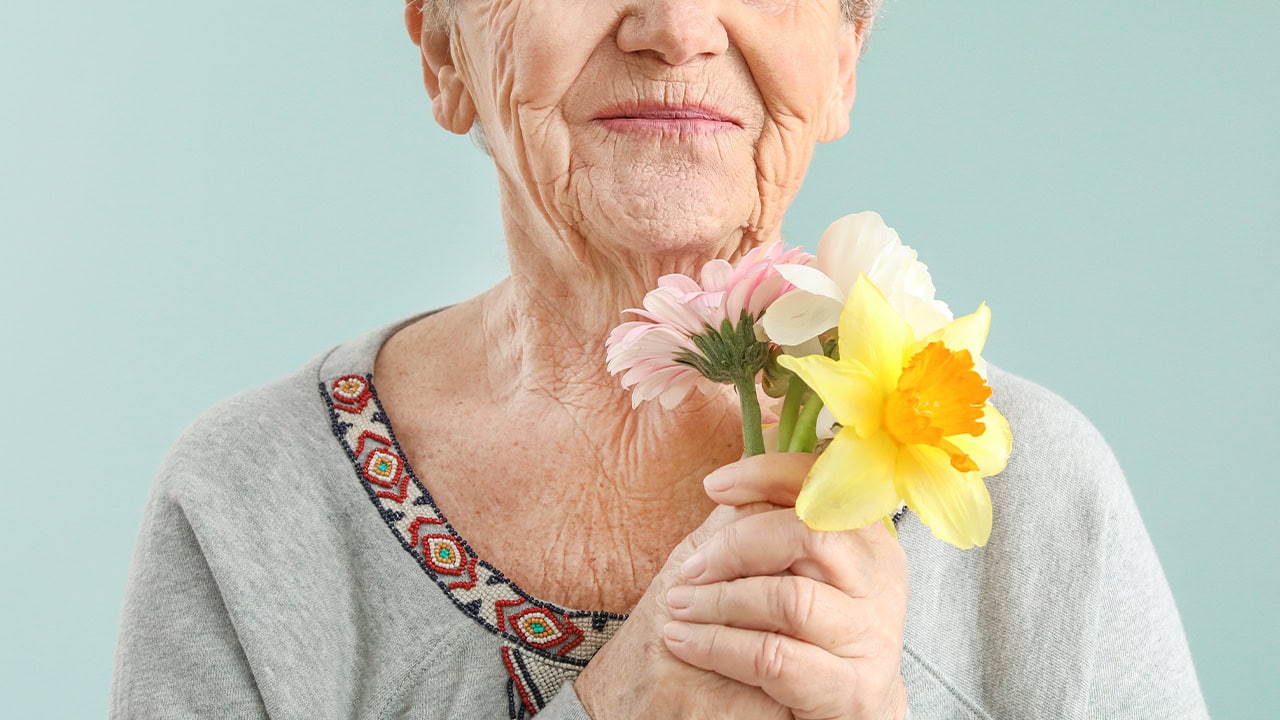 Close-up of a senior woman wearing a sweater holding flowers. Image produced by More Jersey.