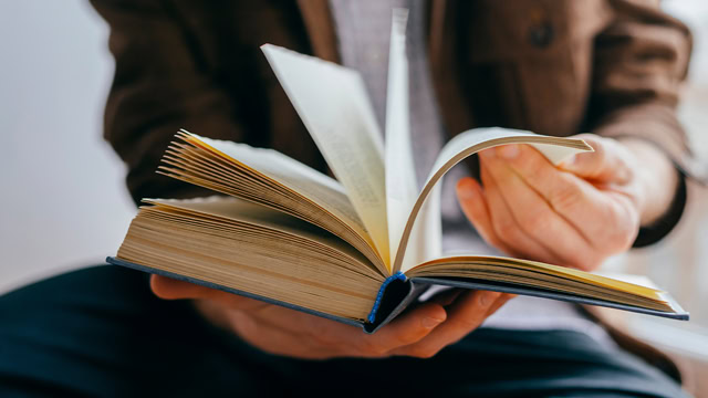 Close-up of a white man flipping through pages of a book.