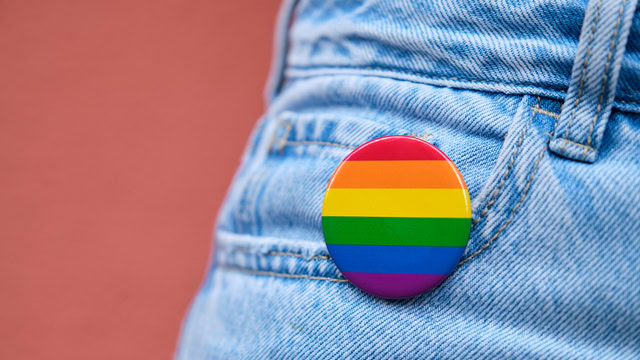 Close-up of blue denim jeans with a rainbow flag pin.