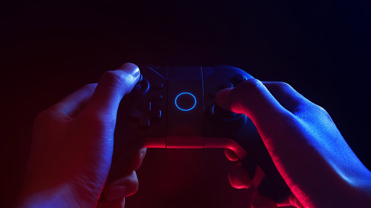 Close-up of esports gamer's hand holding the controller in a dark room with red and blue lighting. Image produced by More Jersey.