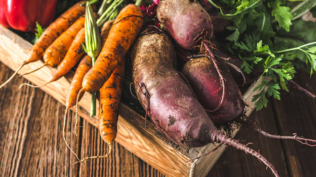  Close-up of fresh farm vegetables like carrots and beets in a wooden box.