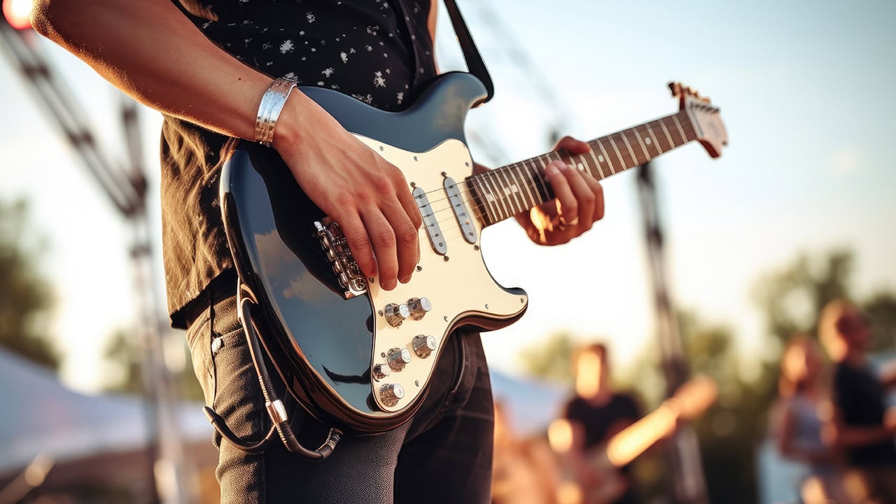 Close-up of guitarist playing electric guitar with band at an outdoor New Jersey music event. Image produced by More Jersey.