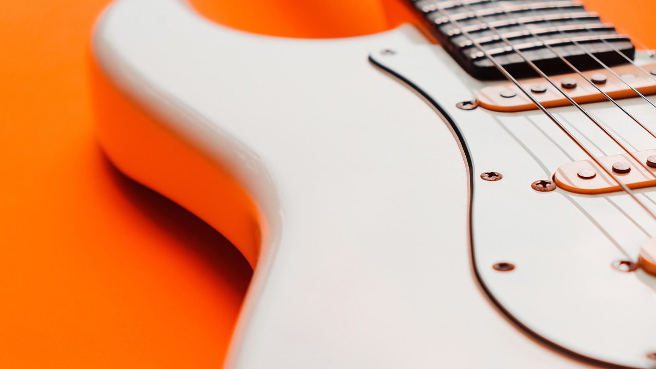 Close-up of white electric guitar on an orange background.