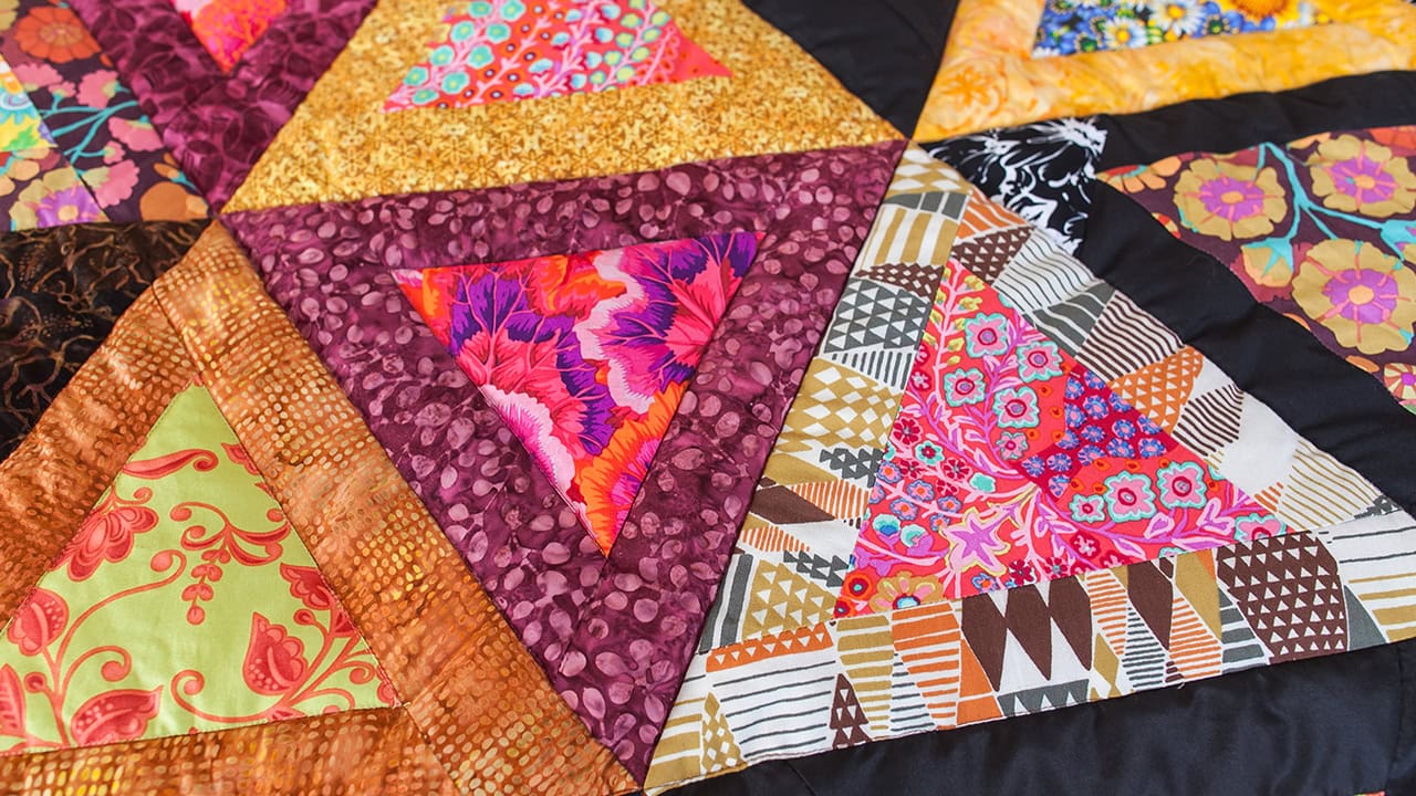 Close-up of a colorful patchwork quilt with various fabrics and stitches. Image produced by More Jersey.