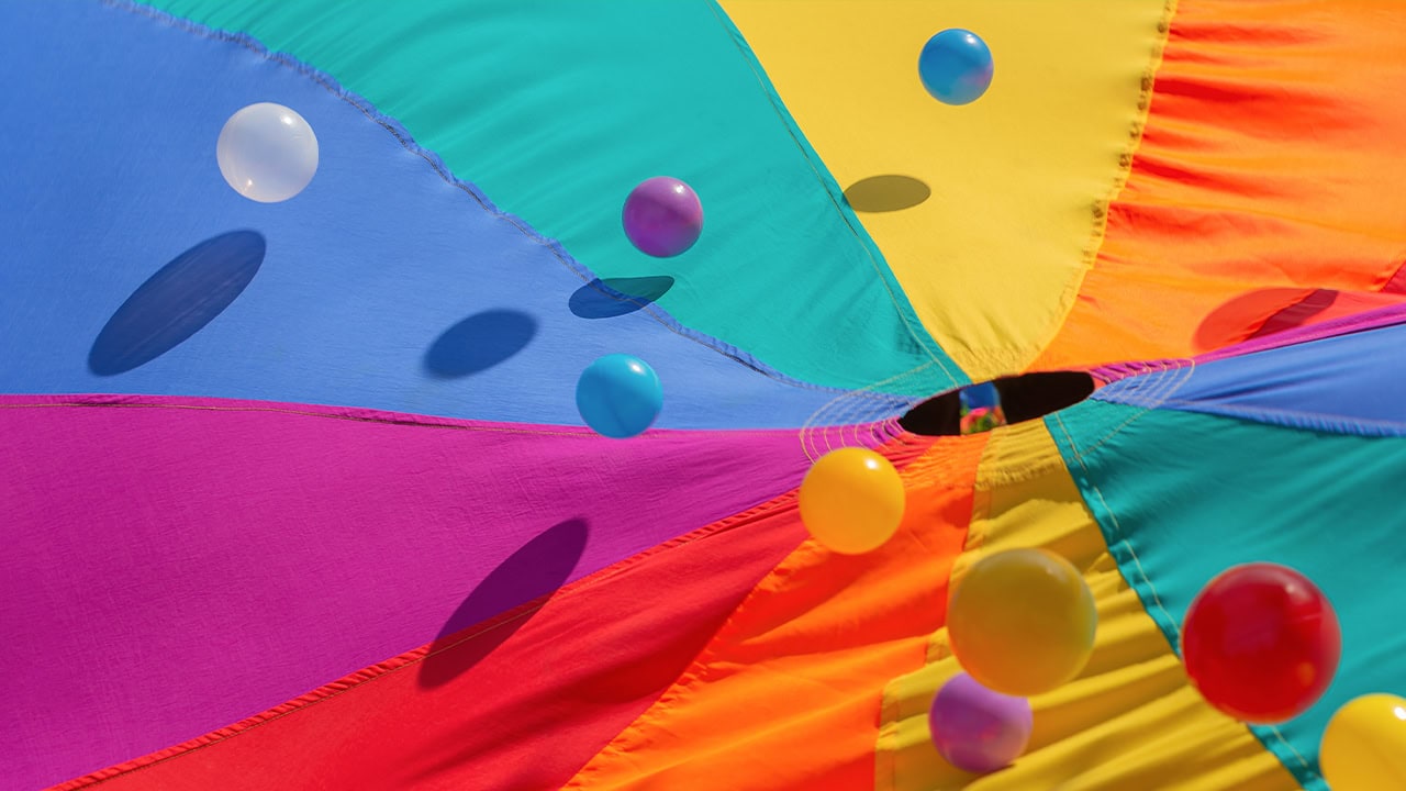 Close-up of rainbow-colored play parachute with colorful bouncing balls. Image produced by More Jersey.