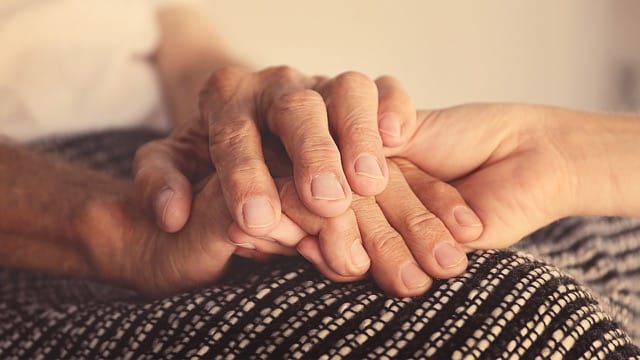 Comforting New Jersey caregiver holding senior hands.