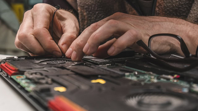 Computer repair technician removing a laptop cooling system from a old computer.