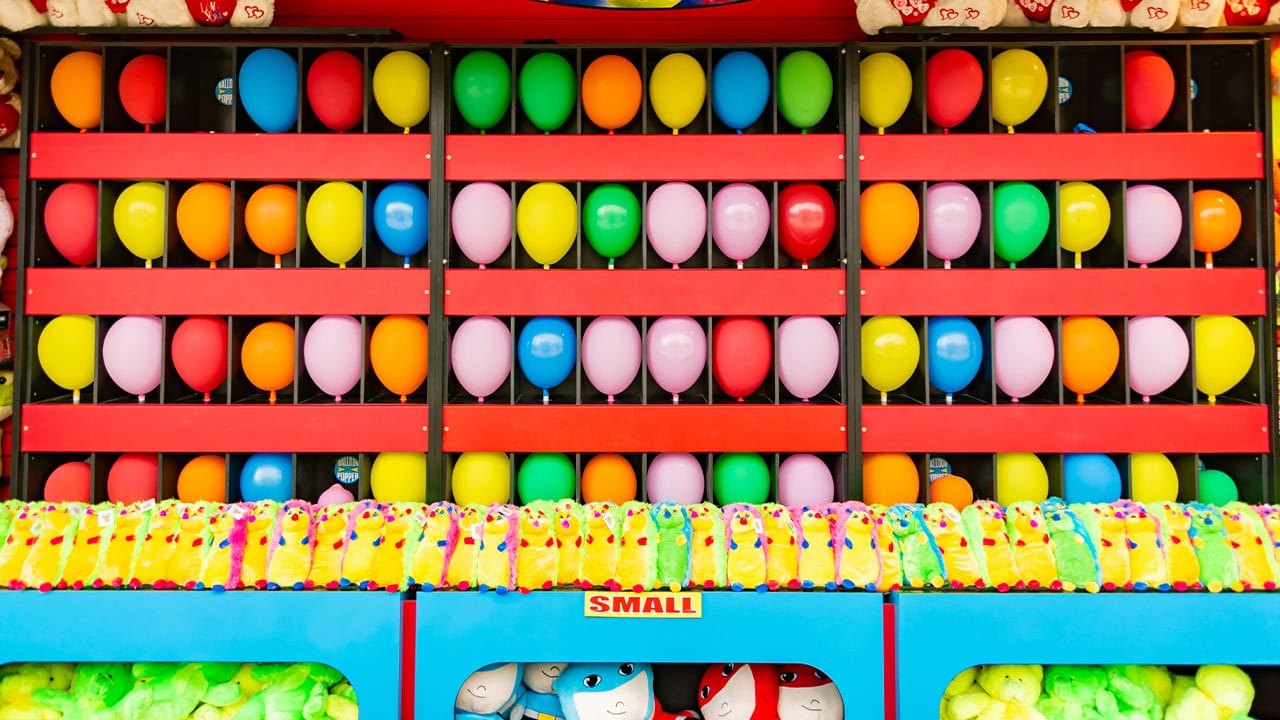 Dart throwing game booth with balloons and prizes at New Jersey carnival. Image produced by More Jersey.