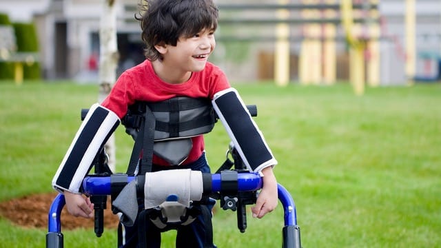 Disabled child smiling while using a walker at New Jersey park.