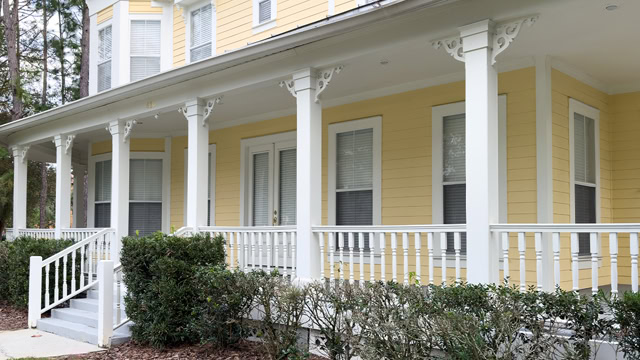 Facade of a large yellow and white colored house with a wraparound porch.