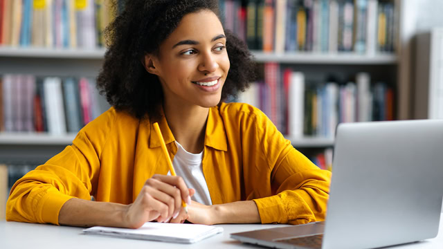 Female African American student doing homework with her laptop at a local library.