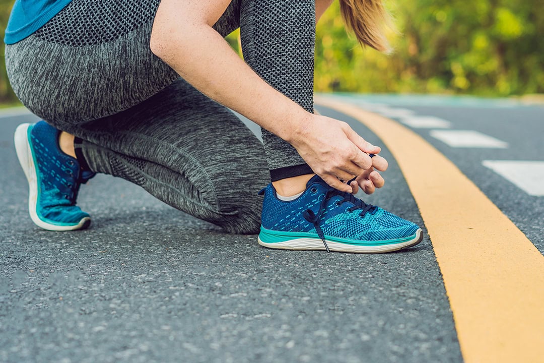 Female runner tying sneaker in preparation for jogging outdoors.