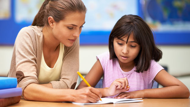 Female white teacher helping a female Latino student with her work in a classroom.