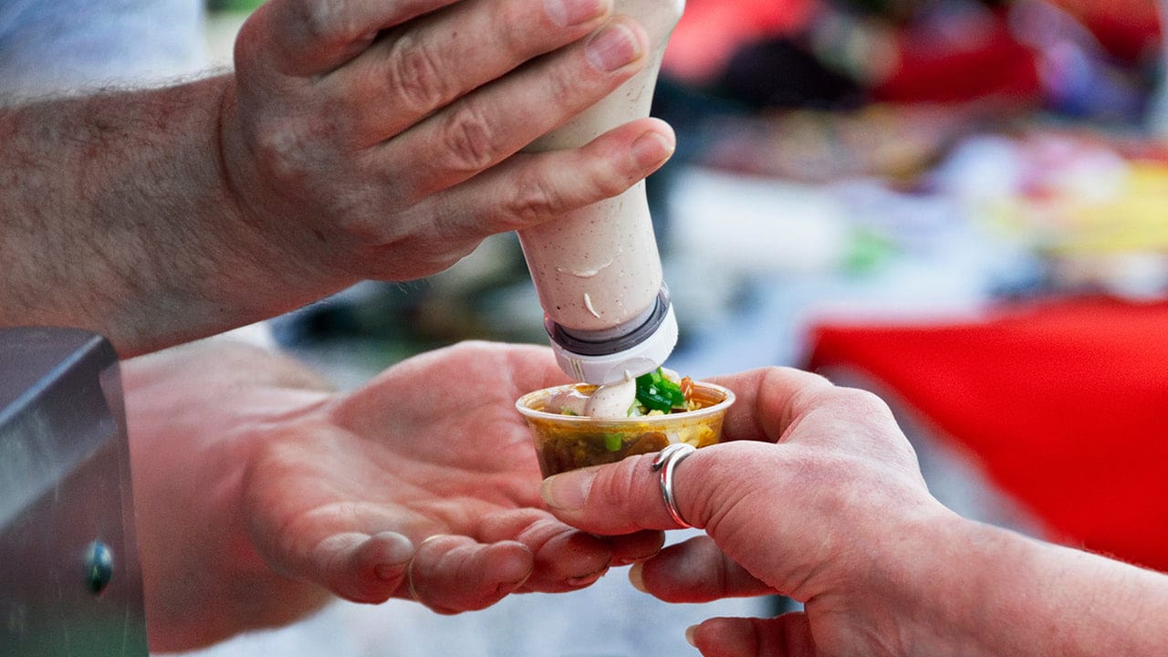 Food vendor adding sauce to patron's food at a New Jersey food tasting event.