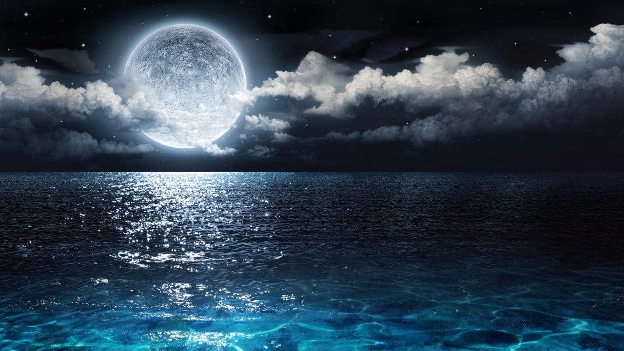 Full moon glowing above a body of water at night.
