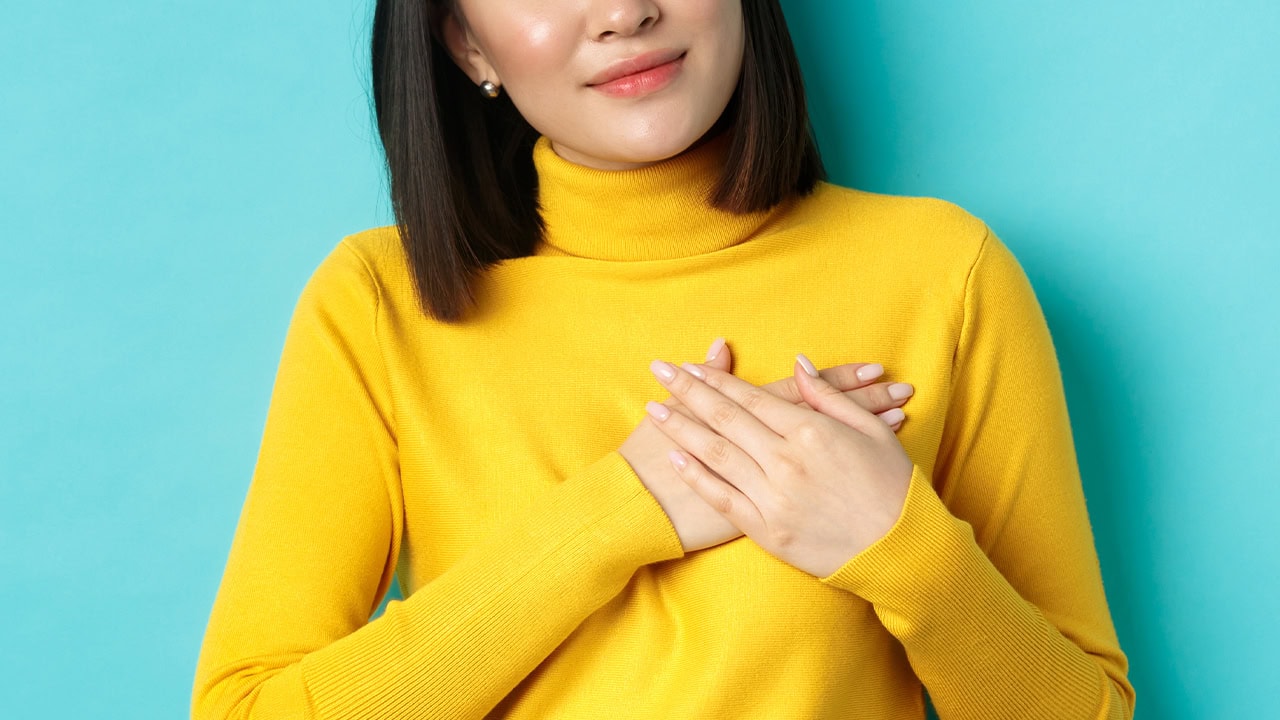 Asian woman with hands over heart gesturing she cares about opportunities to Give Local in New Jersey. Image produced by More Jersey.