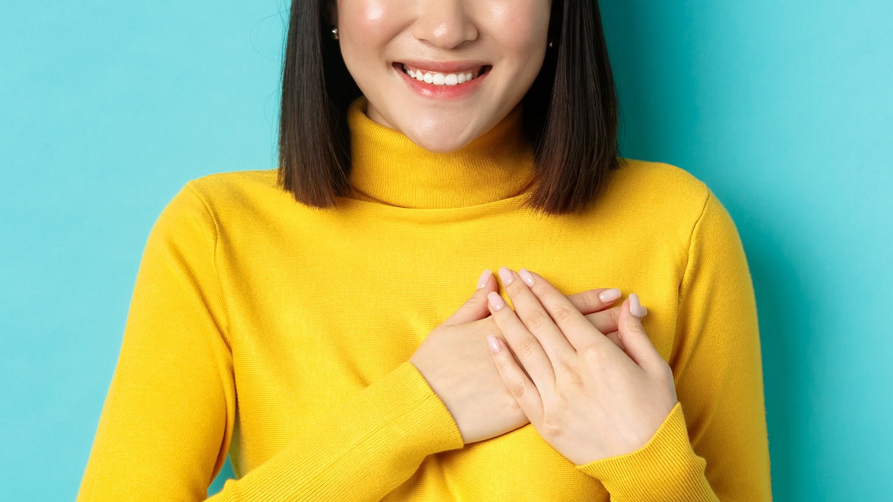 Asian woman with hands over heart gesturing she cares about opportunities to Give Local in New Jersey. Image produced by More Jersey.