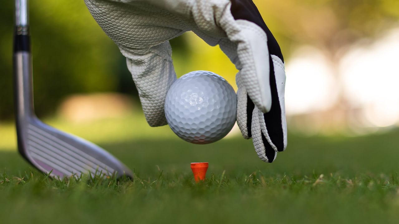 Golf player putting a golf ball on a golf tee. Image produced by More Jersey.