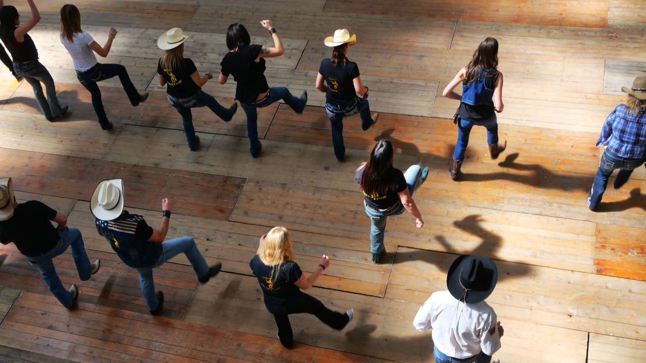 Group of residents country line dancing while wearing cowboy hats and boots.