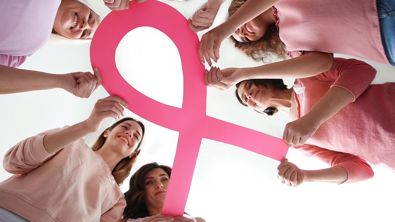 Group of women holding big pink paper ribbon. Image produced by More Jersey.