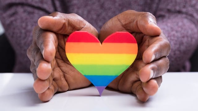 New Jersey resident protecting LGBQT+ rainbow heart with hands.