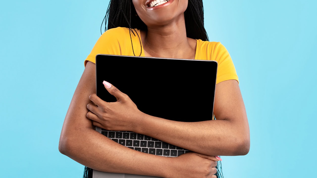 Happy African American female hugging laptop computer.