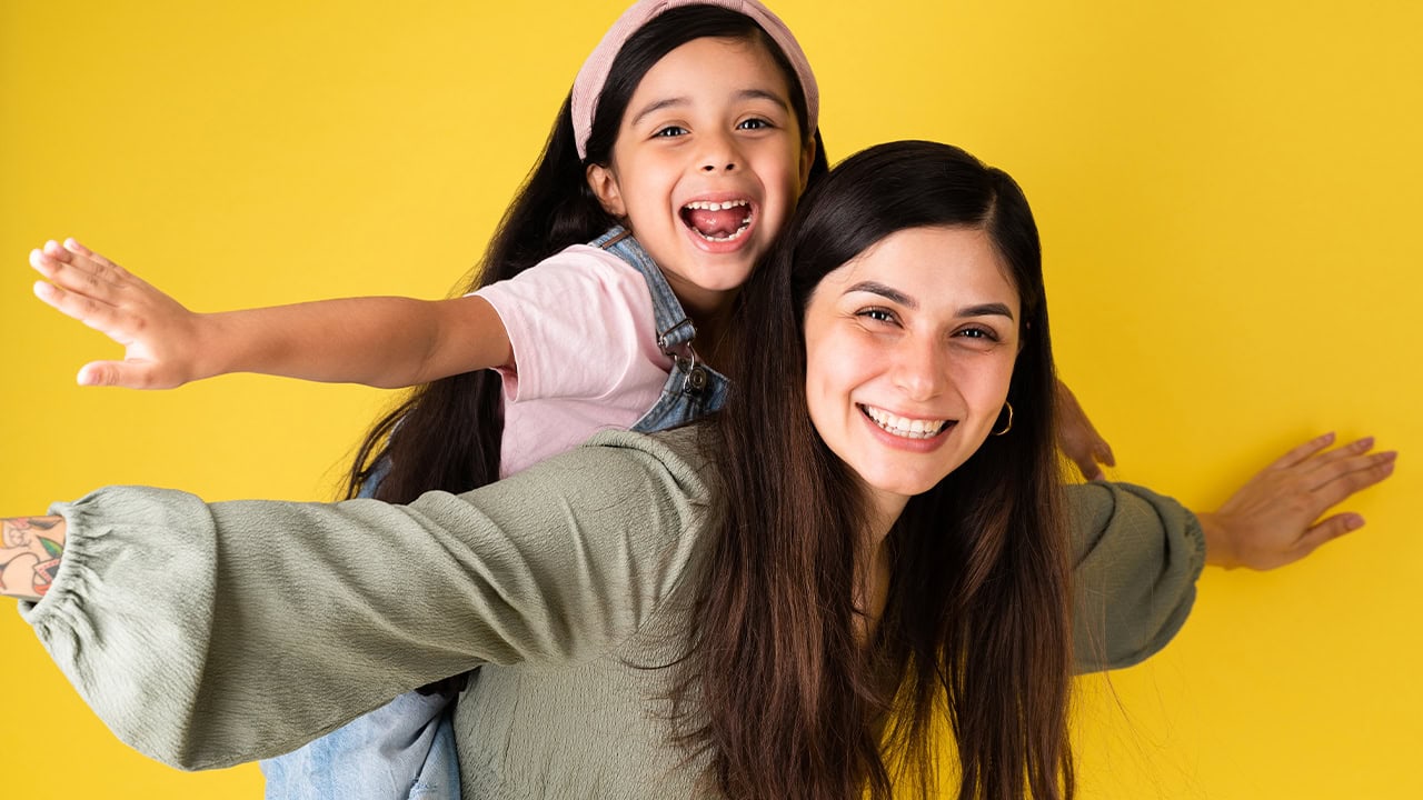 Happy mom and daughter playing in front of a yellow color background. Image produced by More Jersey.