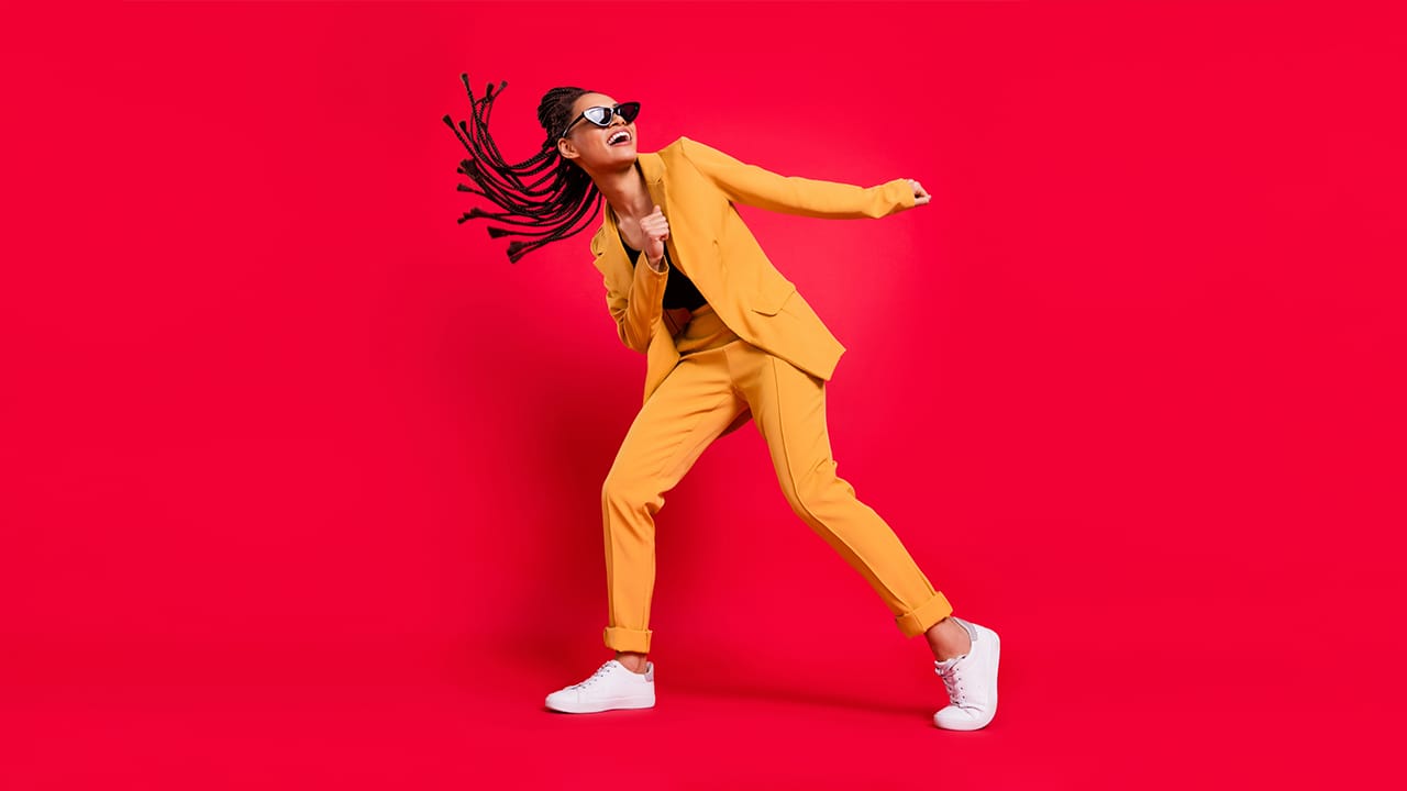 Lady dancing wearing a bright orange suit in front of a vivid red color background.