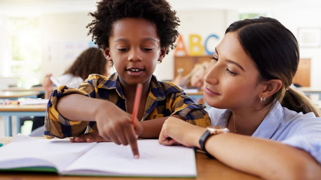 Latino teacher helping African American student studying in a classroom.