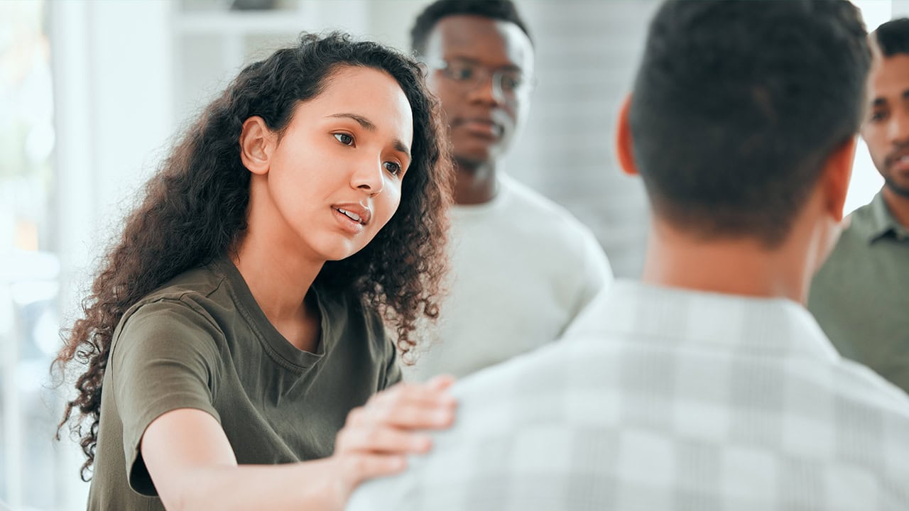 Multiracial woman comforting fellow resident during mental health support group meeting. Image produced by More Jersey.