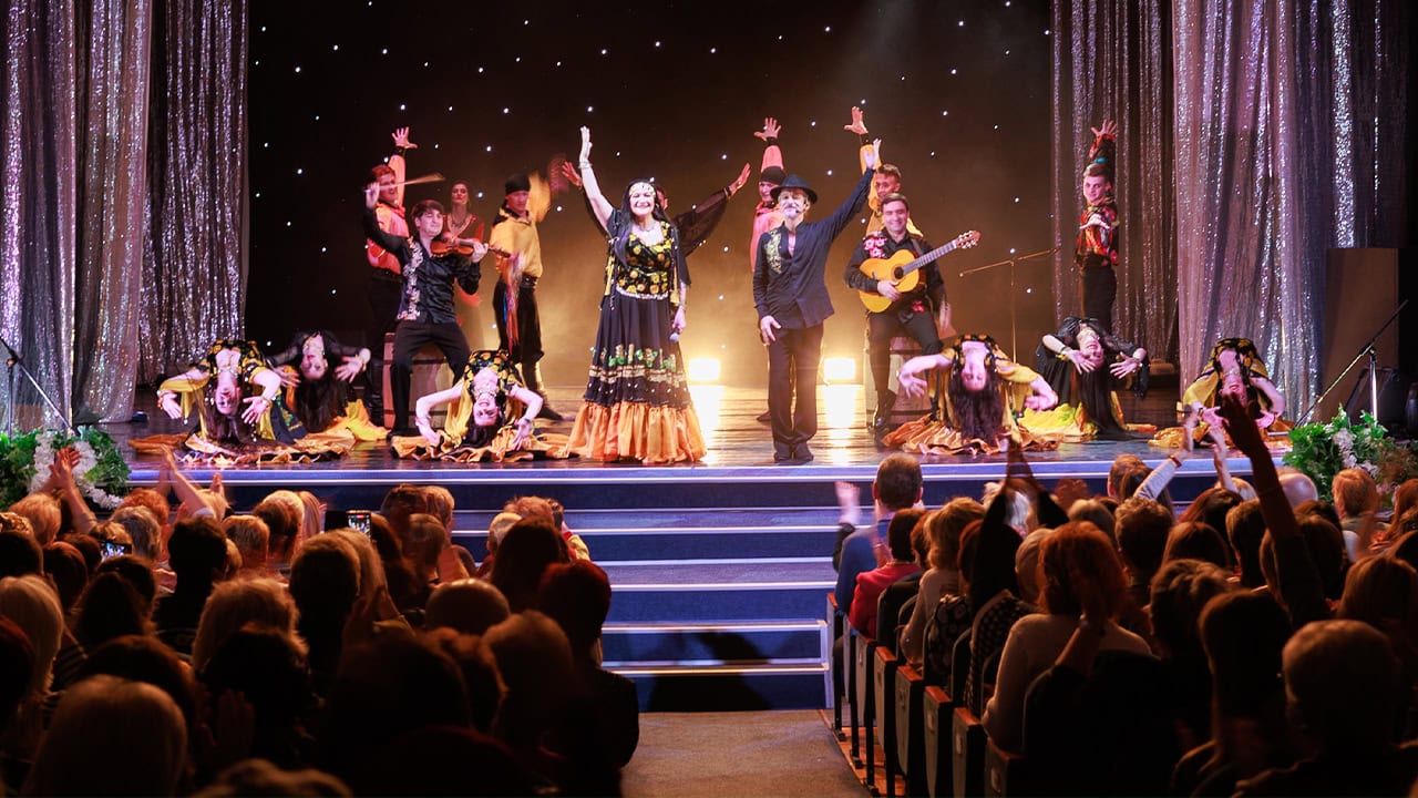 Musicians, singers, and dancers in costumes performing on stage to live audience. Image produced by More Jersey.