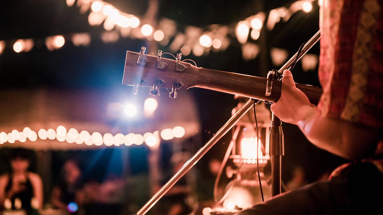 Musician playing guitar at nighttime outdoor music festival.