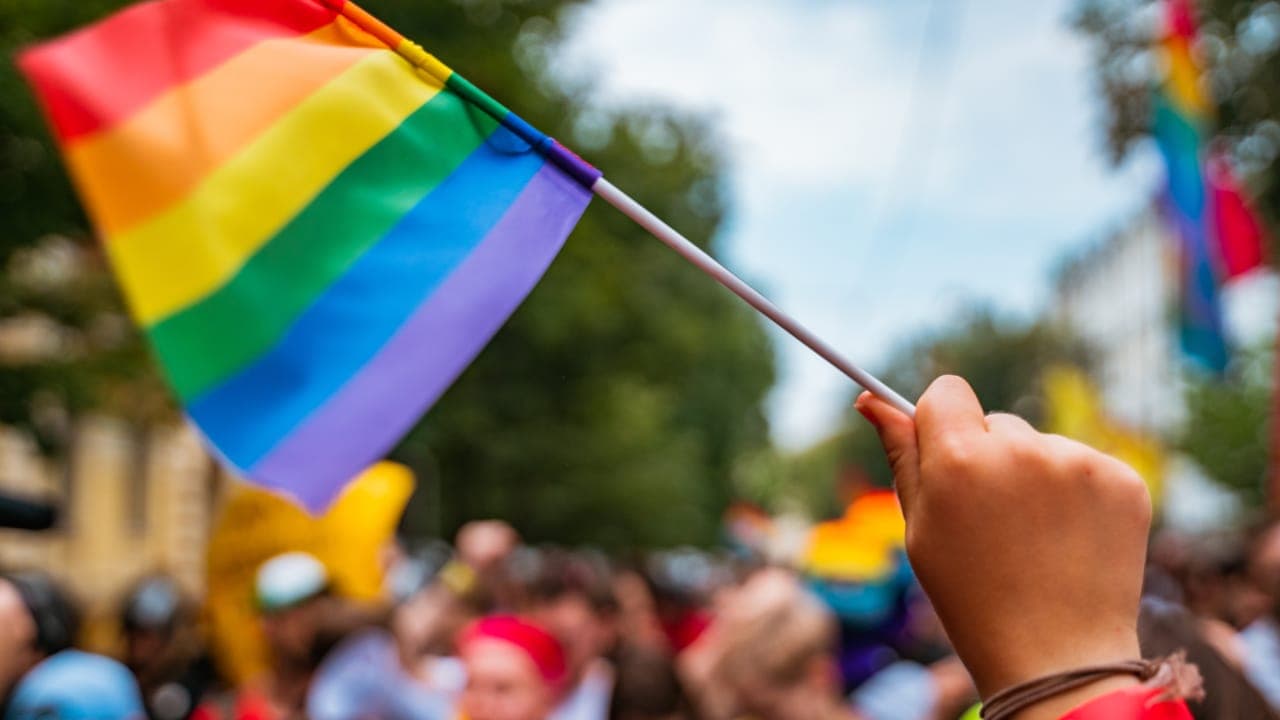 NJ resident holding rainbow flag up at Pride Month celebration. Image produced by More Jersey.