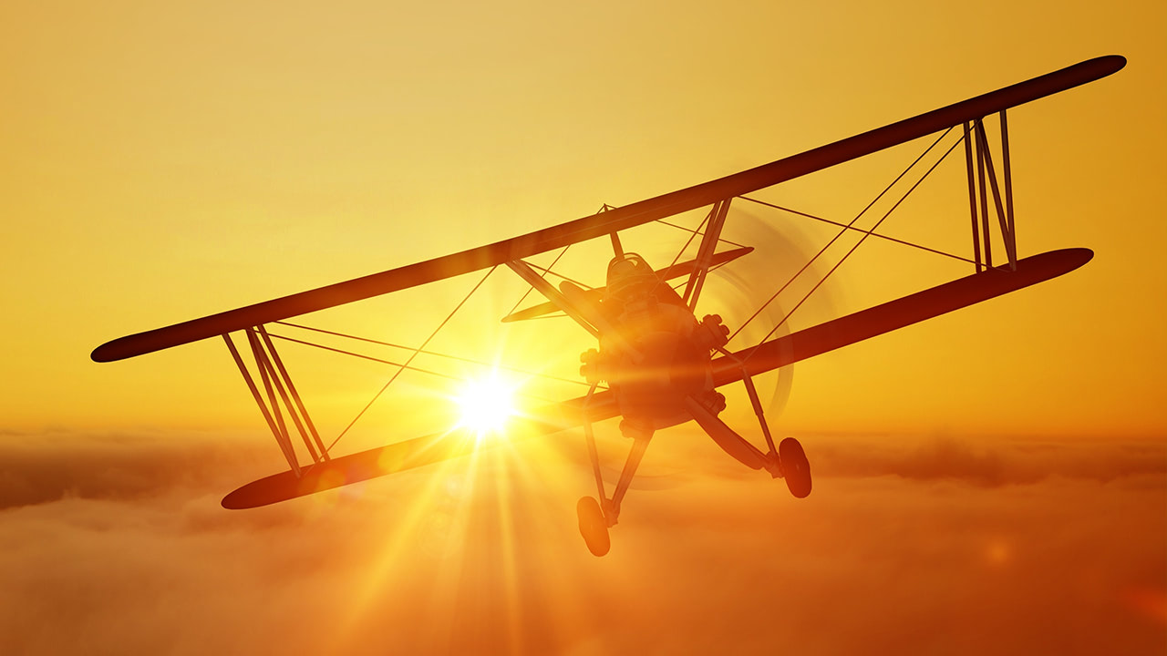 Photo of vintage plane flying with sunset in background.