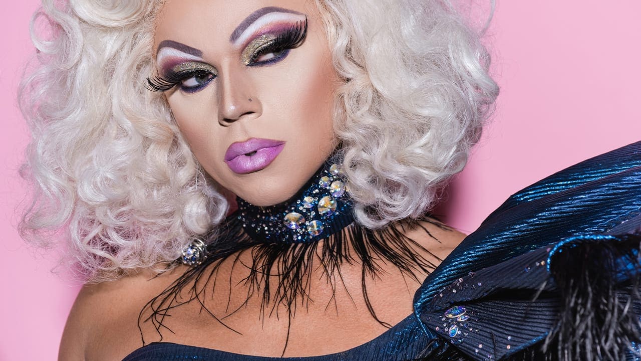 Portrait of transgender person in blonde wig and shiny necklace.