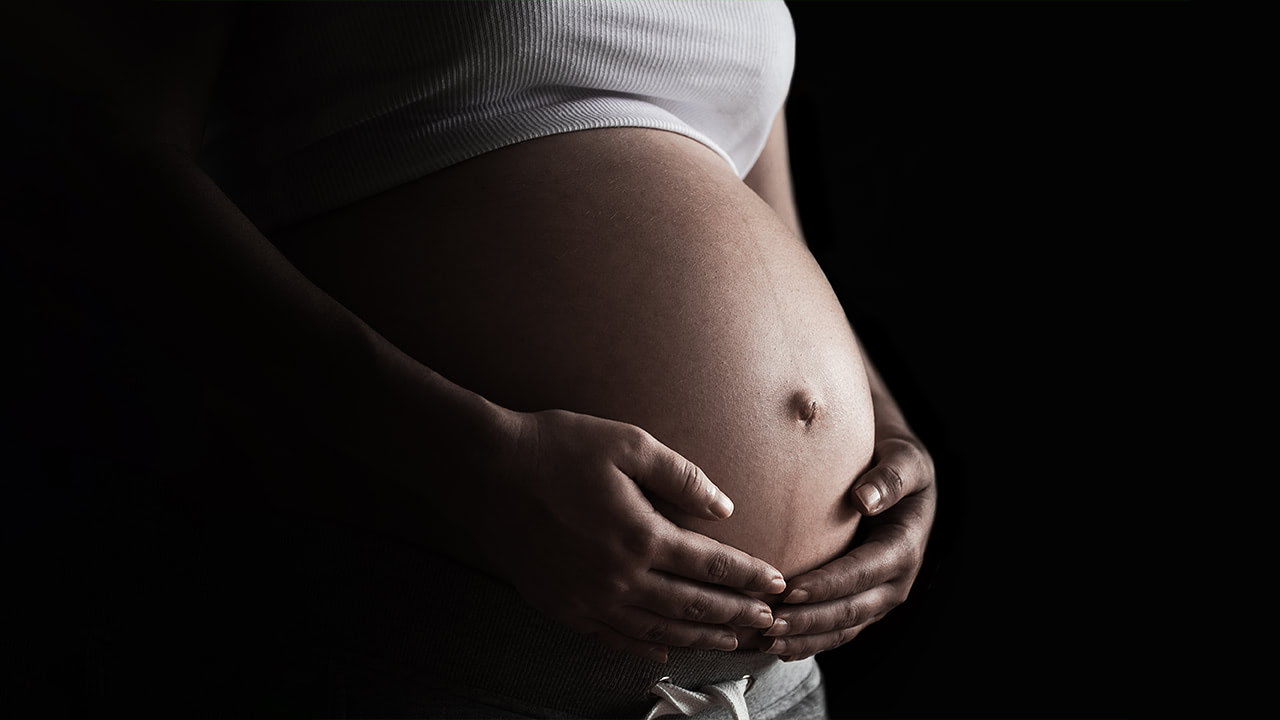 Pregnant African American woman holding her exposed belly in a dark room representing black maternal and infant health in New Jersey.