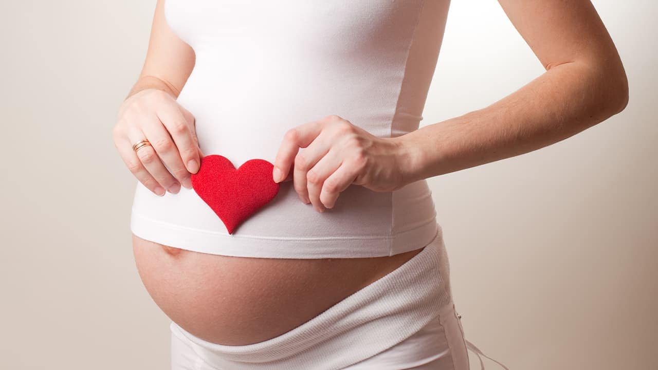 Pregnant New Jersey woman holding heart-shaped toy over her belly.