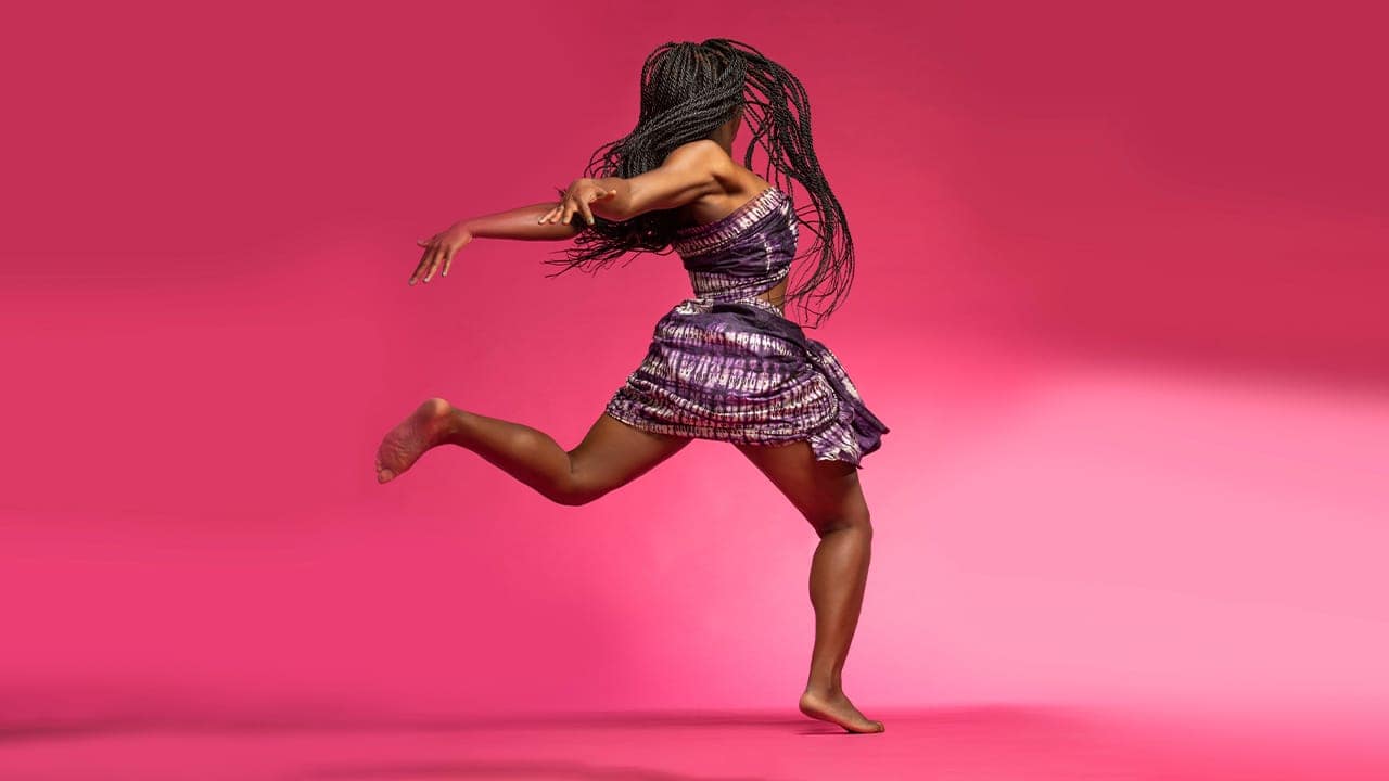 Professional dancer performing traditional African dance routine against a colorful pink background at New Jersey dance performance.