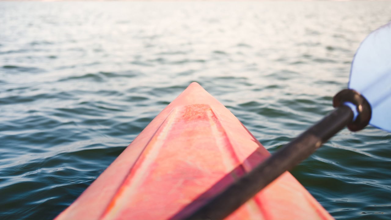 Red kayak canoe floating in water with paddle on top. Image produced by More Jersey.