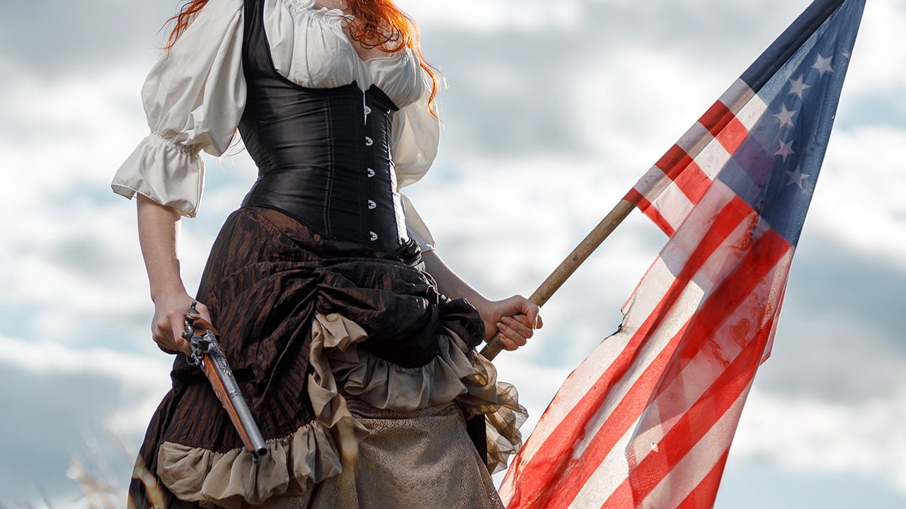 Reenactment portrait of a female patriot fighter with a gun and flag in hand.